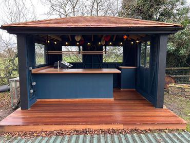 Outdoor bar setup with wooden counter and string lights in a garden.