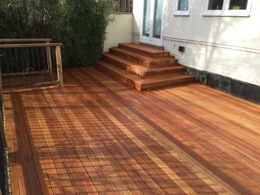 A clean wooden deck with built-in stairs and railing near a white building.