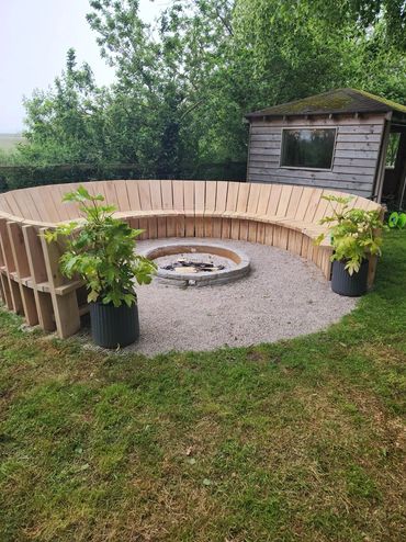 Circular wooden bench around a fire pit in a garden.