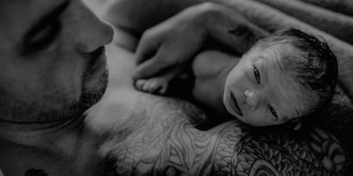 Newborn in his dad' tattooed arms. Nashville newborn nurse postpartum care