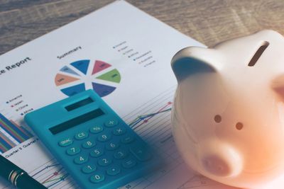Piggy bank, calculator, pen, and financial reports on a wooden desk.