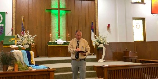 Man reading book inside church with green cross lit up.