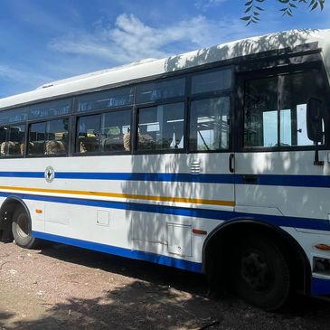 White bus with blue and yellow stripes parked under a clear sky.