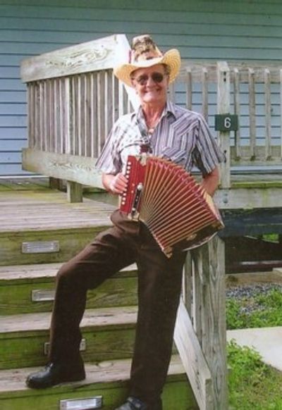 An elderly man with a cowboy hat playing an accordion on wooden steps.
