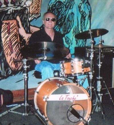Man wearing sunglasses playing a drum set indoors.