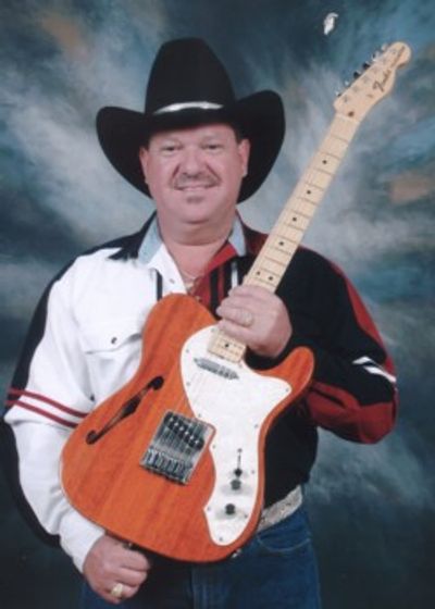 Man in cowboy hat holding a wooden electric guitar.