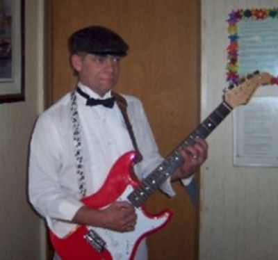 Man in formal attire playing a red electric guitar indoors.