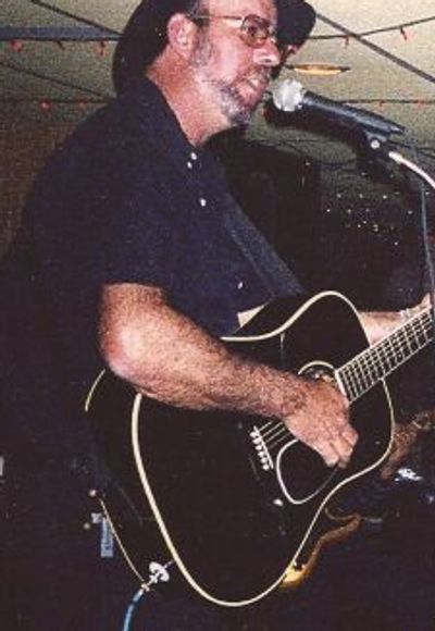 Man in hat playing acoustic guitar and singing into microphone.