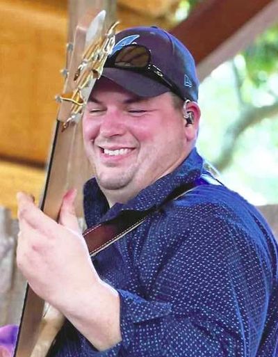 Man smiling while playing a bass guitar outdoors.
