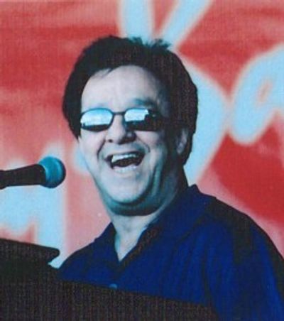 Man smiling while speaking or singing into a microphone.