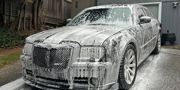 Car covered in foam during a wash in a driveway.