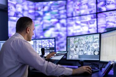 Man monitoring multiple surveillance screens in a security control room.
