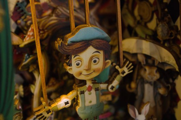 Wooden puppet with a blue cap and suspenders on strings.