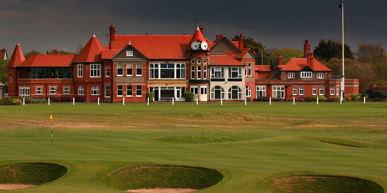 Historic red brick building by golf course under stormy sky.