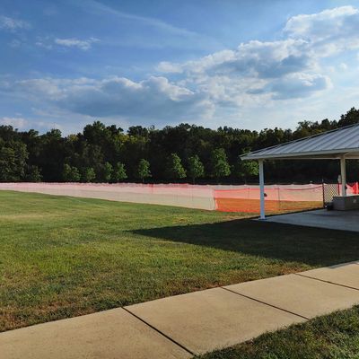 A grassy field with orange safety fencing and a pavilion under a partly cloudy sky.