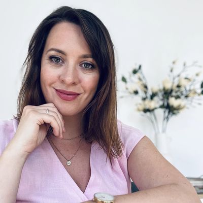 A smiling woman in a pink top posing indoors with a floral background.