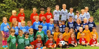 Group of children wearing colorful Oxford sports shirts, posing outdoors.