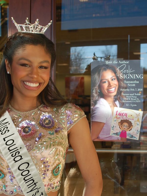 Miss Louisa County's smiling pageant winner stands by a book signing poster.