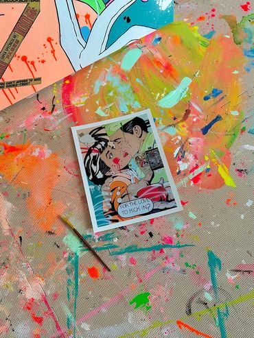 A comic-style artwork on a colorful, paint-splattered canvas with a paintbrush nearby.