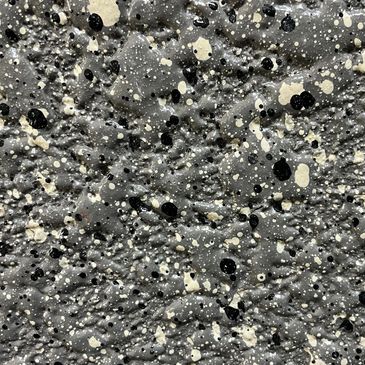 Textured surface with black and white paint splatters on a gray background.