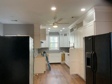 Modern kitchen under renovation with white cabinets and black appliances.