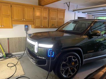 A Rivian electric SUV charging in a garage with wooden cabinets.