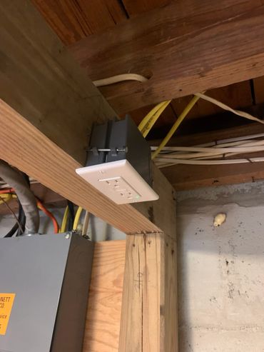 Electrical outlet box installed sideways on a wooden beam in a basement ceiling.