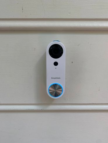 A SimpliSafe video doorbell mounted on a white door.
