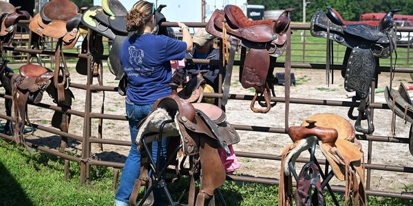 a woman organizing saddles on a fence