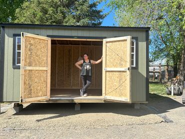 Woman standing in the doorway of a new wooden shed on a sunny day.