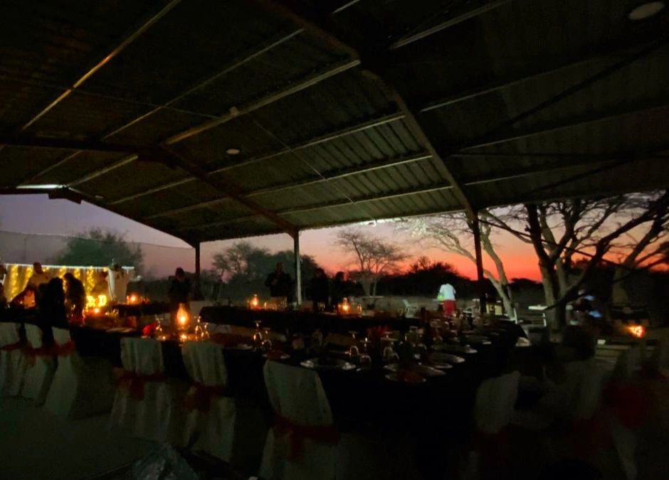 Outdoor evening event with candlelit tables and sunset in the background.