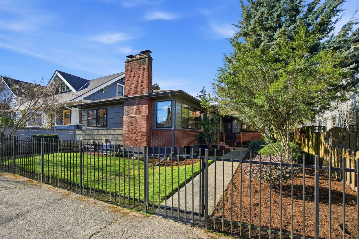 Charming brick and siding house with a well-kept lawn and black metal fence.