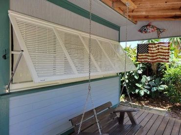 Outdoor porch with a swinging bench, hinged window shutters, and American flag decor.