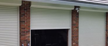 Brick house with partially open white roller shutters by a pool.