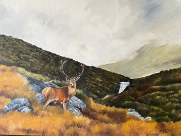 A majestic stag stands on rocky terrain with hills and a waterfall in the background.