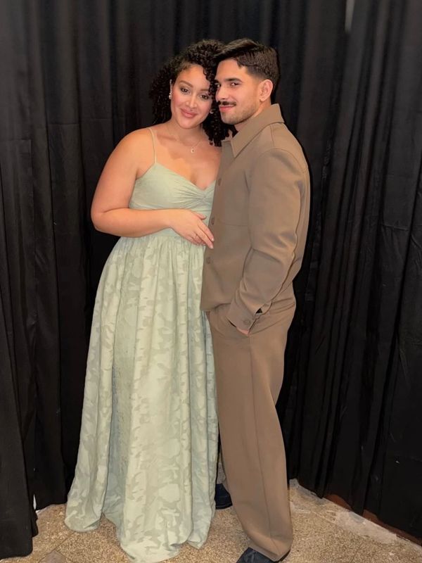 A couple poses together in elegant attire against a black curtain backdrop.