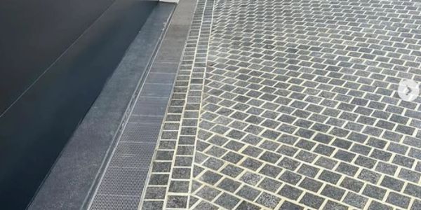Paved ground with dark and light stone pattern near a metal grate.