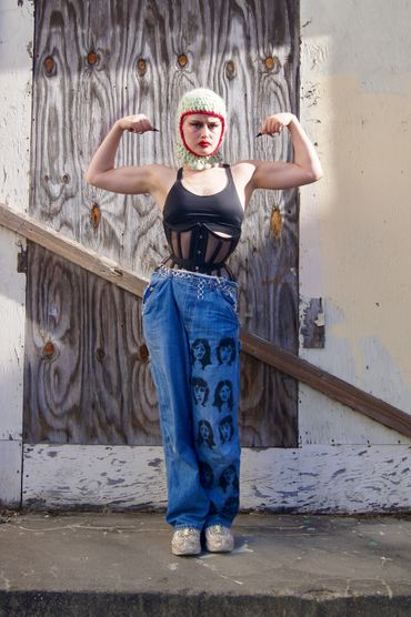 Person in a knitted hood flexing muscles in artistic denim pants.