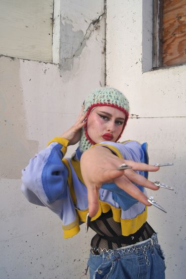 Fashion-forward individual with dramatic makeup and silver claw-like nails striking a bold pose.