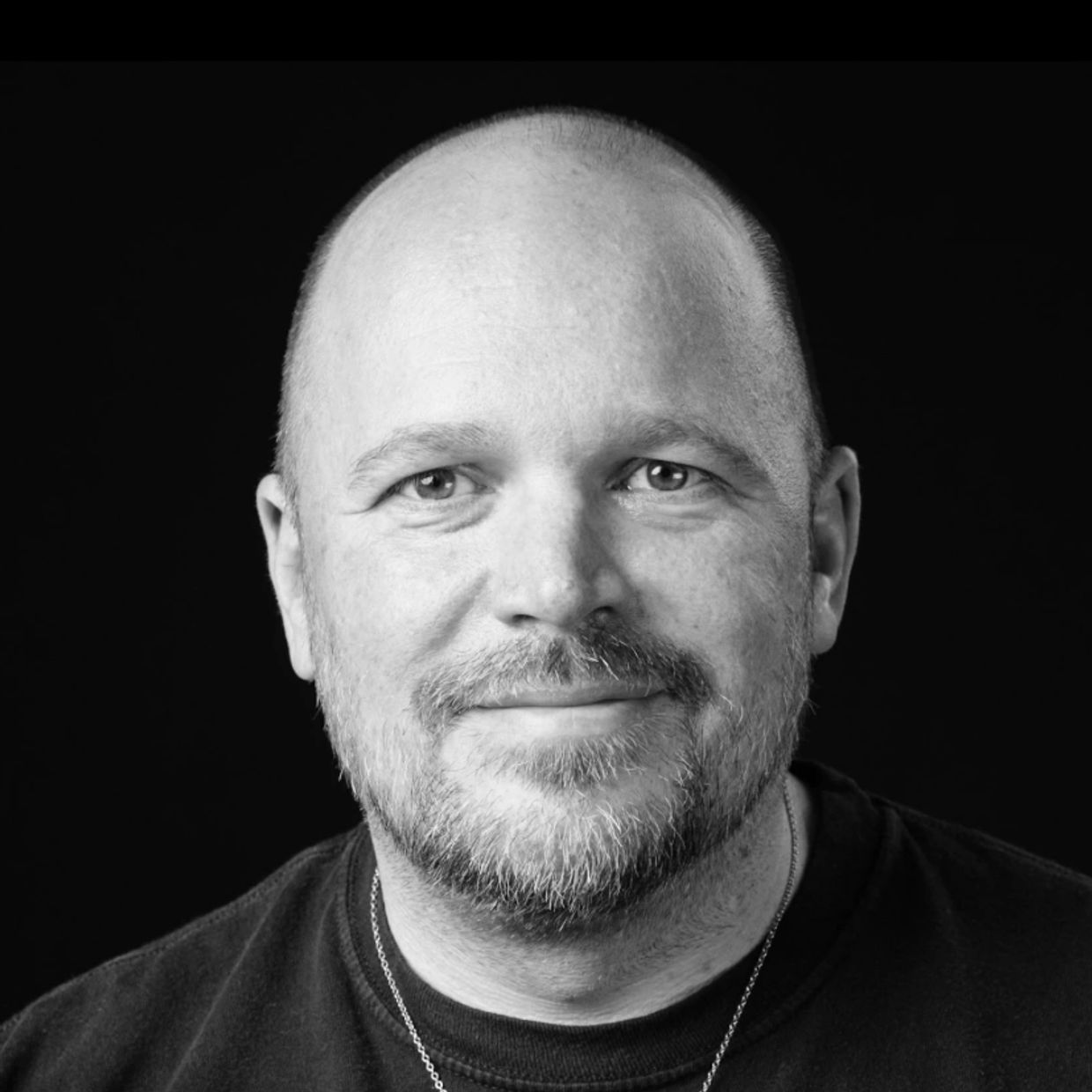 Black and white portrait of a smiling bald man with a beard.