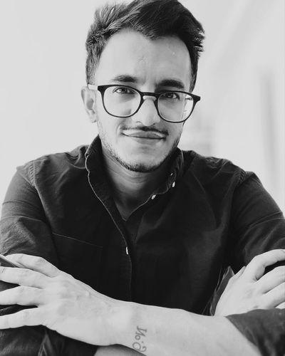 Black and white portrait of a man wearing glasses and a dark shirt, with arms crossed.