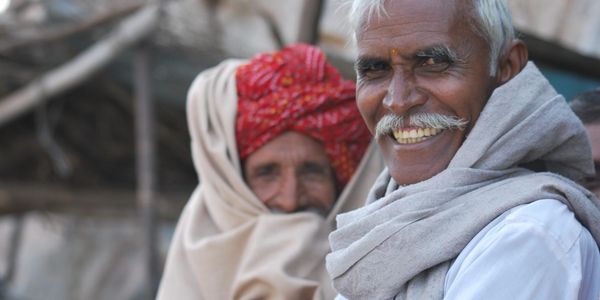 Two elderly men from India, one smiling warmly with a white mustache.