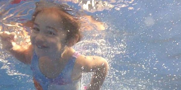 A girl smiling underwater in a swimming pool.