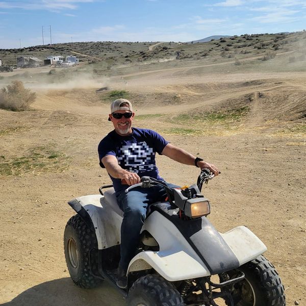 Man riding ATV on a dirt trail on a sunny day.