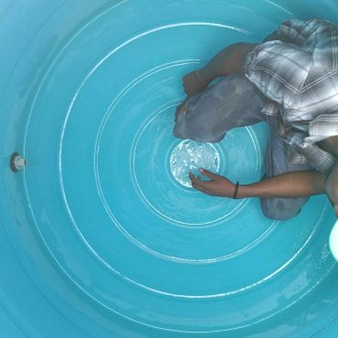 Person kneeling inside a large blue plastic container.
