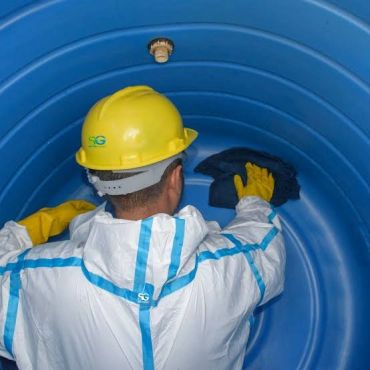 Worker cleaning inside a large blue tank with protective gear.