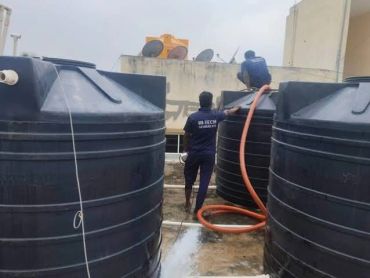 Workers cleaning water tanks on a rooftop.