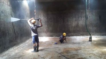 Workers cleaning a large, empty concrete tank.