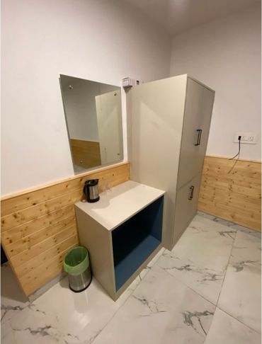 Minimalist room corner with a cabinet, mirror, kettle, and trash bin.