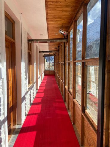 Long corridor with red carpet and wooden window frames overlooking snowy mountains.